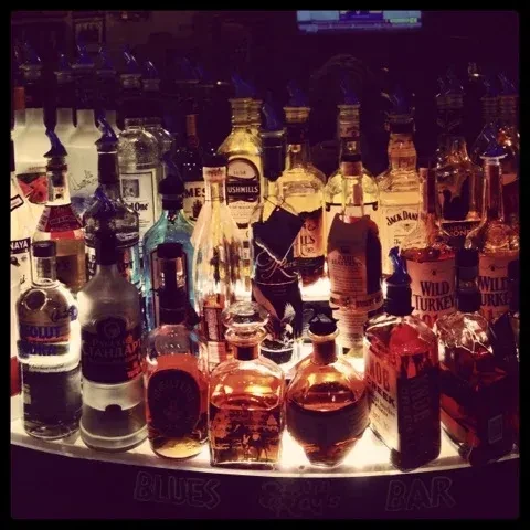 Warmly lit, well-stocked BLUES BAR shelf with liquor bottles and pour spouts.