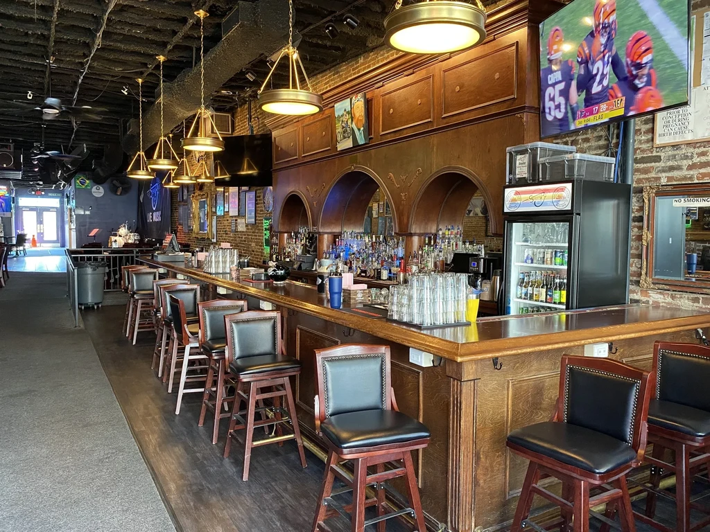 Empty bar interior with wooden counter, stools, liquor shelves, football on TV.