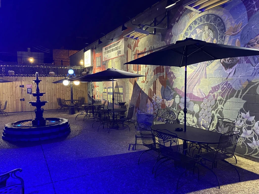 Empty restaurant patio at night with blue-lit fountain and colorful mural.