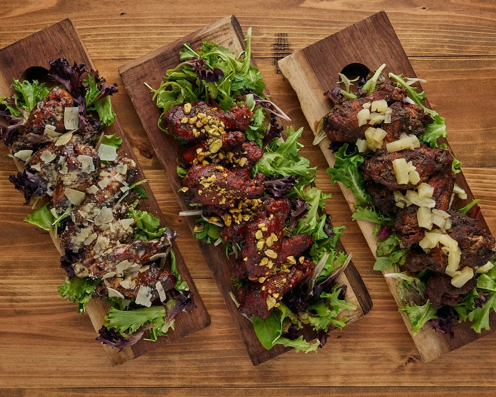 Overhead view of three wooden boards with different chicken wings on greens.