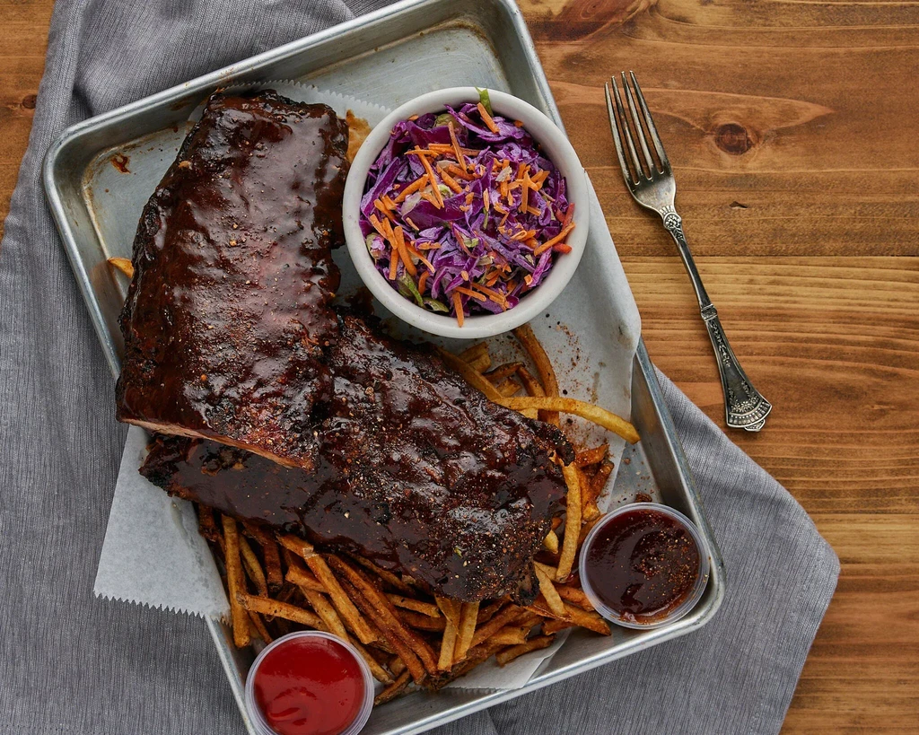 BBQ ribs, fries, coleslaw, sauces on a tray with a fork.