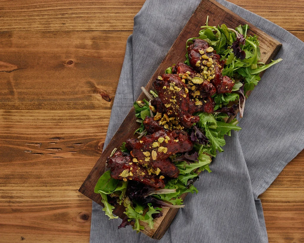 Overhead view: dark glazed meat with pistachios and mixed greens.