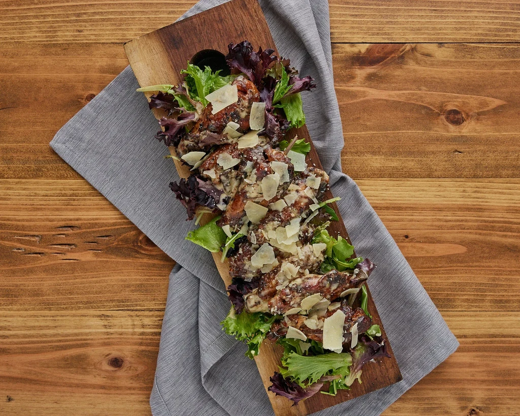 Grilled meat skewers with creamy sauce, Parmesan, and salad on a wooden board.