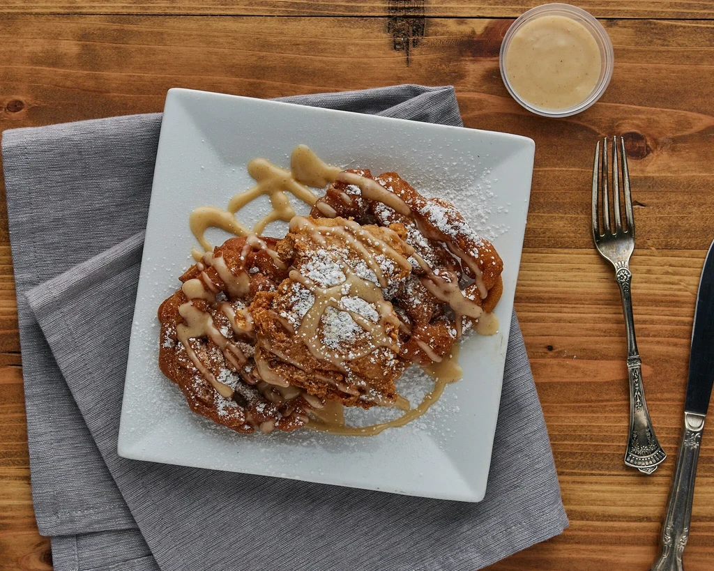 Golden-brown fritters drizzled with sauce and powdered sugar.