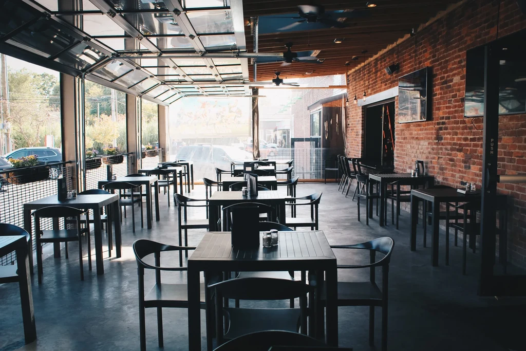 Modern restaurant interior: glass doors, dark tables, exposed red brick wall.