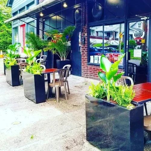 Outdoor restaurant seating with planters, green plants, and dark brick facade.