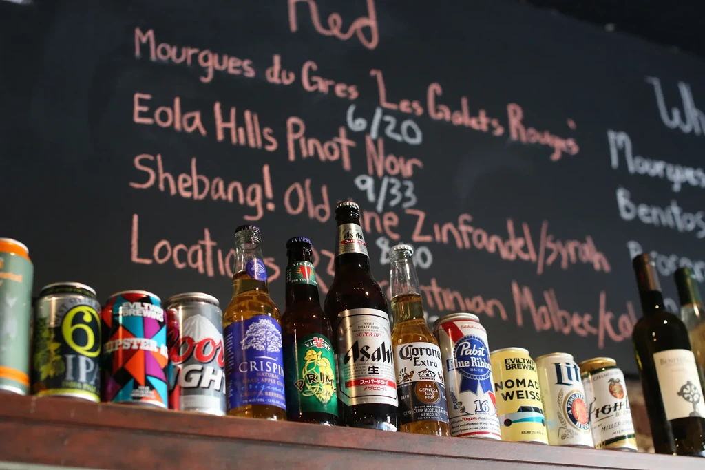 Various beers, ciders, and wines on a bar with a chalk menu.