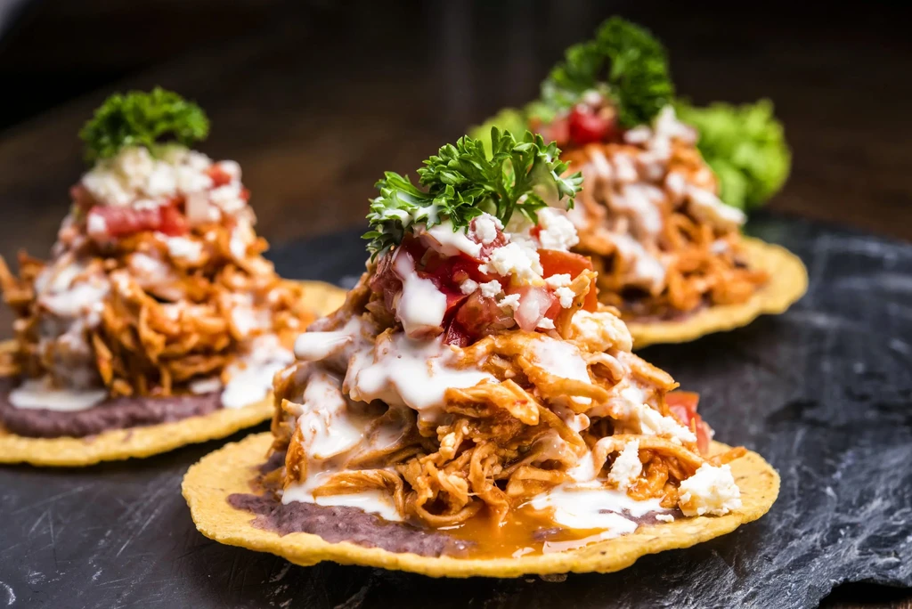 Three plated crispy chicken tostadas with sauce, cheese, tomatoes, parsley.