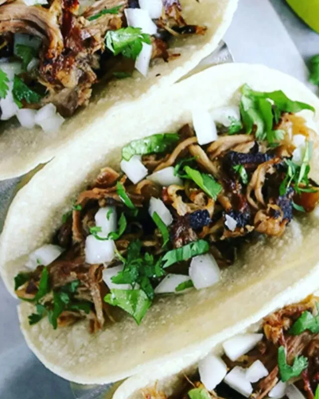 Three tacos with shredded meat, diced onions, and fresh cilantro.