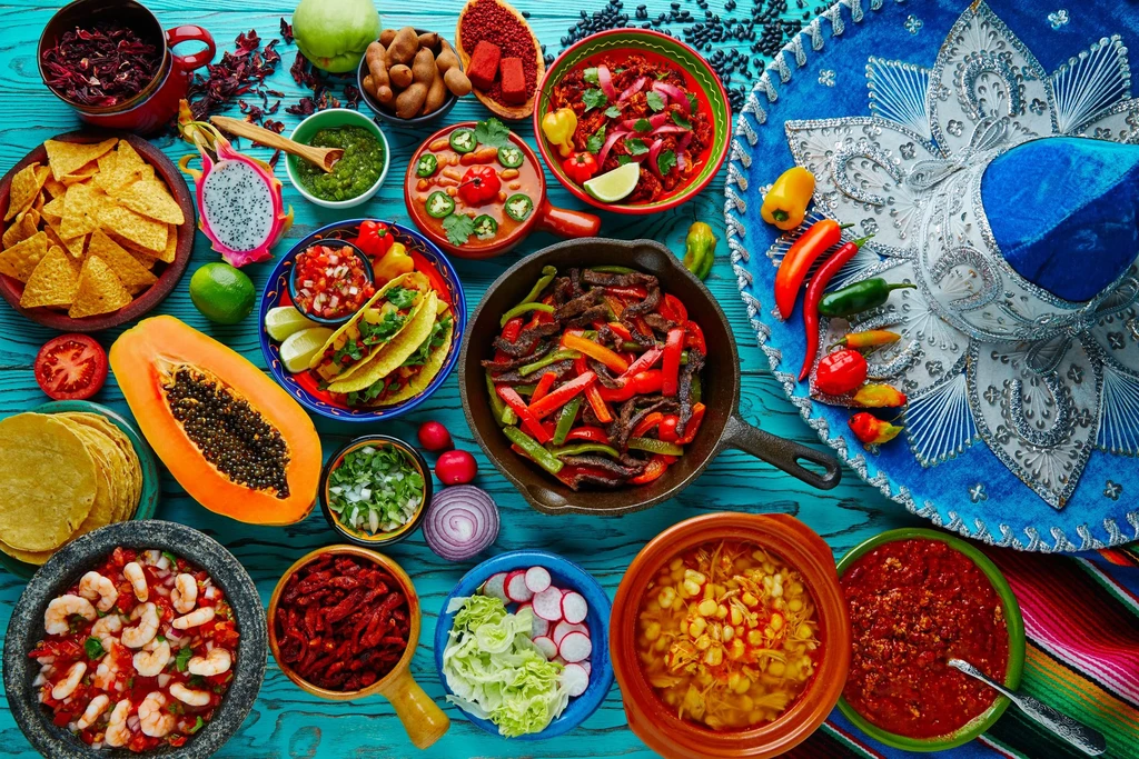 Overhead view of colorful Mexican food spread with sombrero on turquoise table.