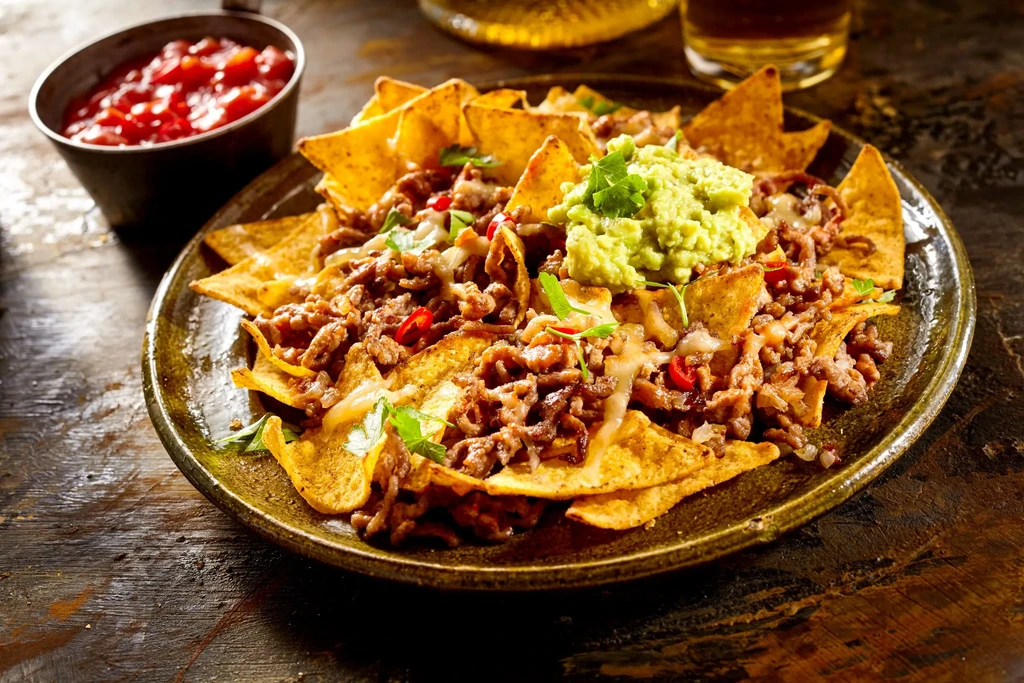 Close-up of fully loaded nachos with meat, melted cheese, guacamole, salsa.