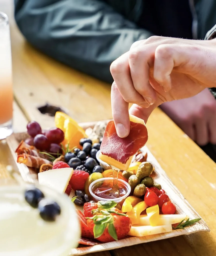 Hand picks prosciutto-wrapped cheese from charcuterie board, honey drips.
