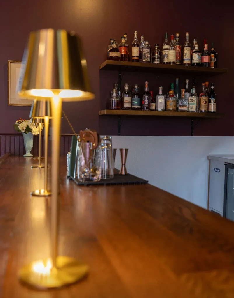 Polished wooden bar with warm lighting, bar tools, and liquor display.