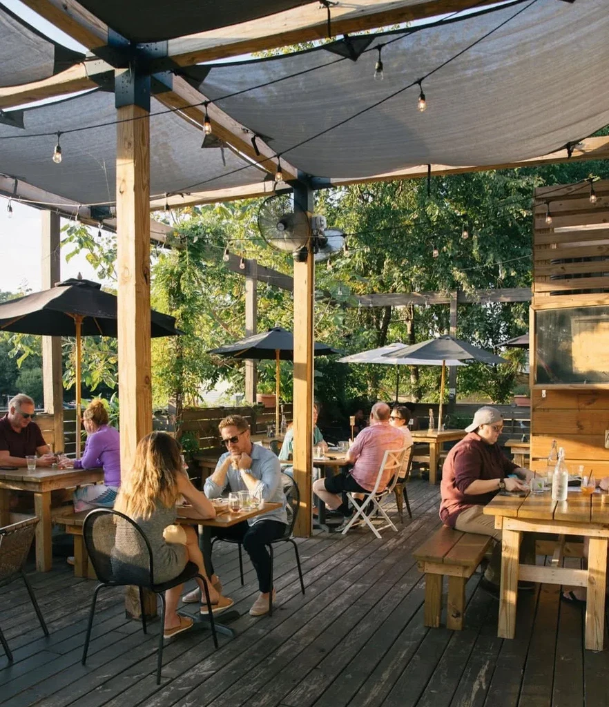 Outdoor restaurant patio with shaded canopies, string lights, and diners.