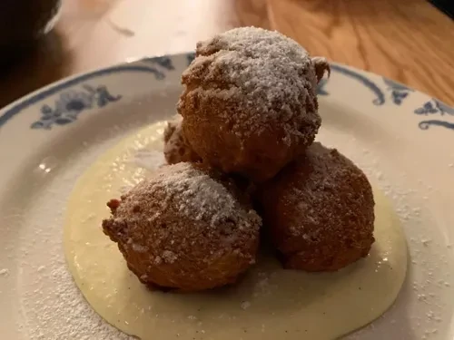 Stacked, sugar-dusted fried dough balls on creamy sauce, floral plate.