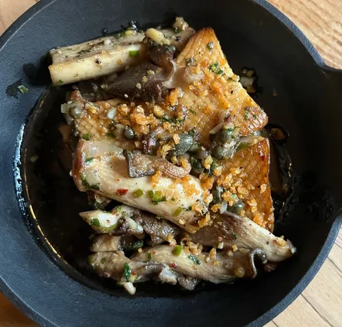 Close-up of glossy sautéed mushrooms with herbs, capers, and crispy bits.