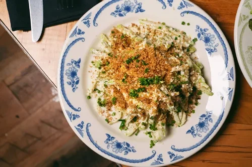 Plated creamy green dish topped with breadcrumbs and fresh herbs.
