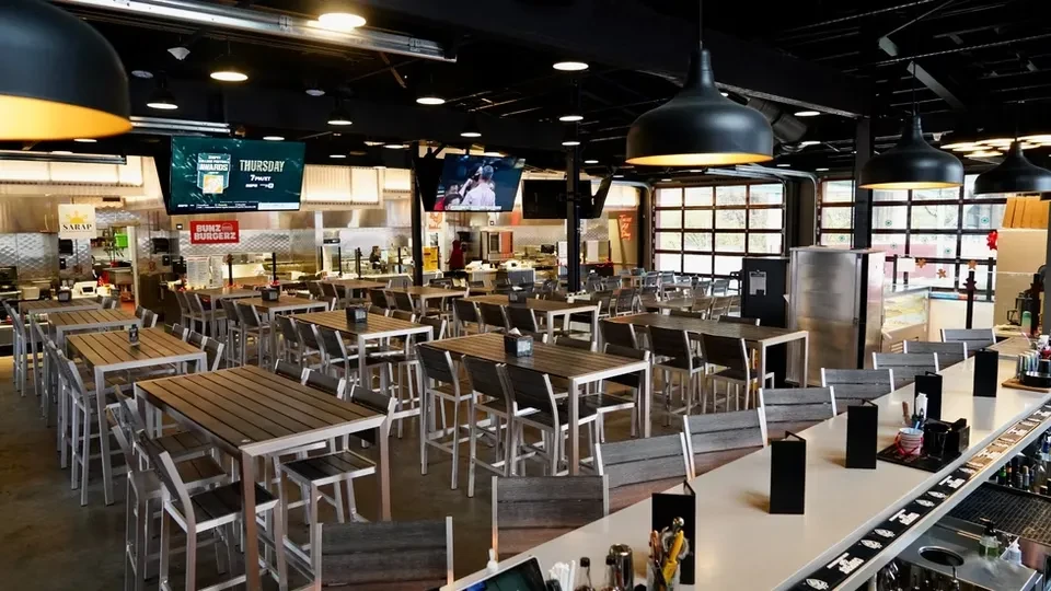 Industrial restaurant with high-top tables, a bar, open kitchen, and TVs.