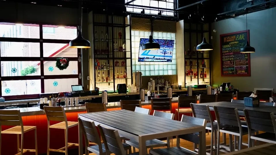 Modern restaurant bar with communal tables, sports TV, and chalkboard menu.