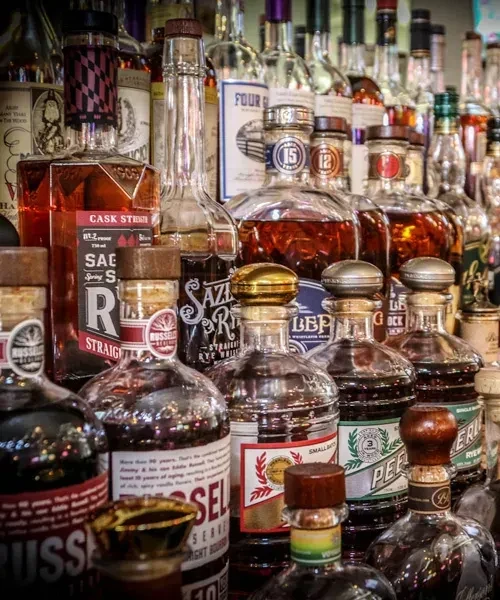 Close-up of numerous amber whiskey and bourbon bottles with visible labels.