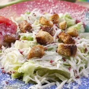 Salad with lettuce, croutons, cheese, and tomato on a colorful plate.