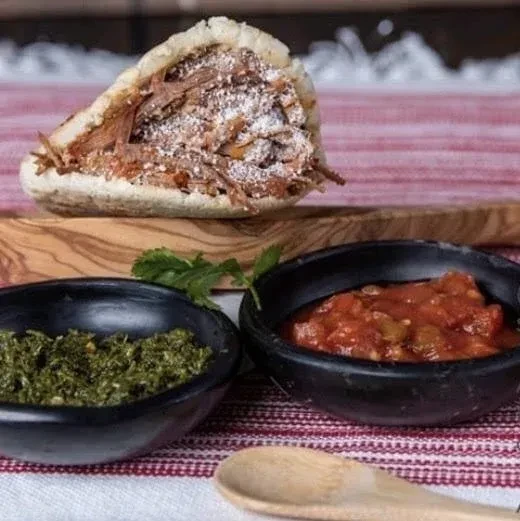 Split arepa filled with meat and cheese, served with two sauces.