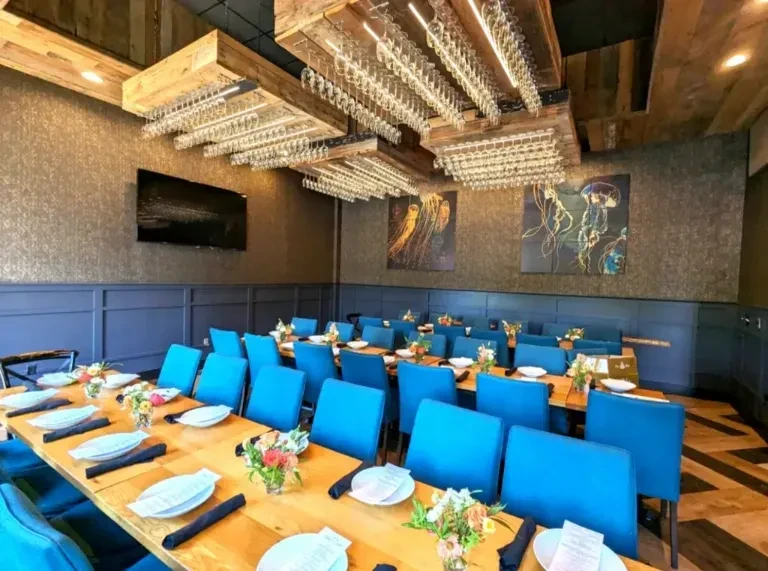 Restaurant dining room with set wooden tables, turquoise chairs, suspended wine glasses.