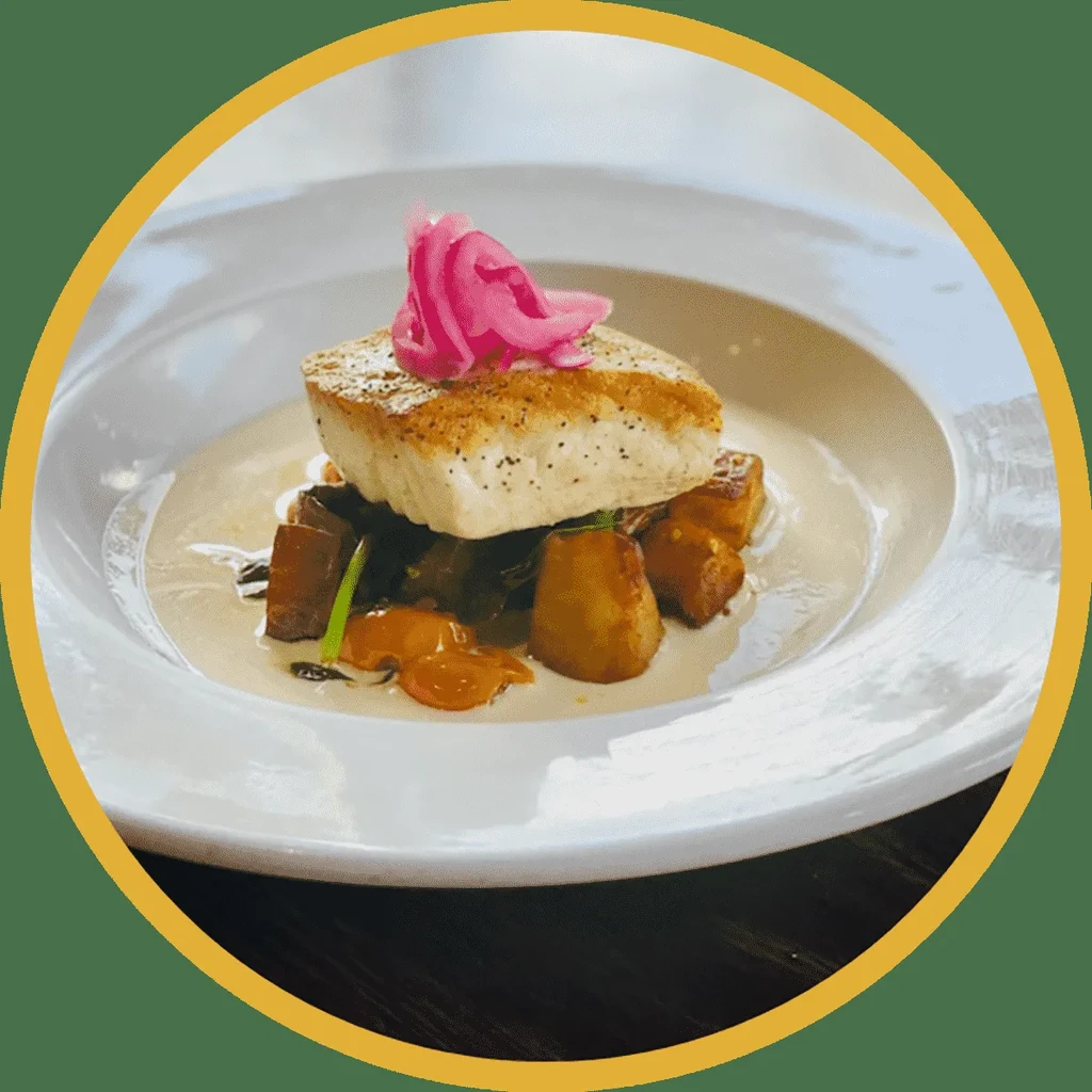 Plated seared fish, vegetables, creamy sauce, and pink pickled onions.