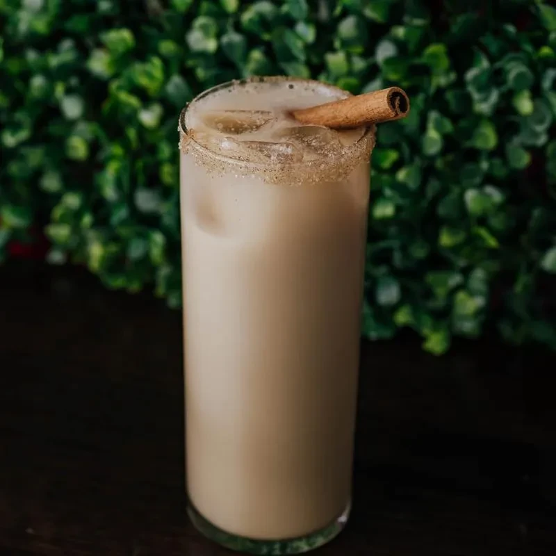 Horchata in a glass with ice, cinnamon stick, and sugared rim.