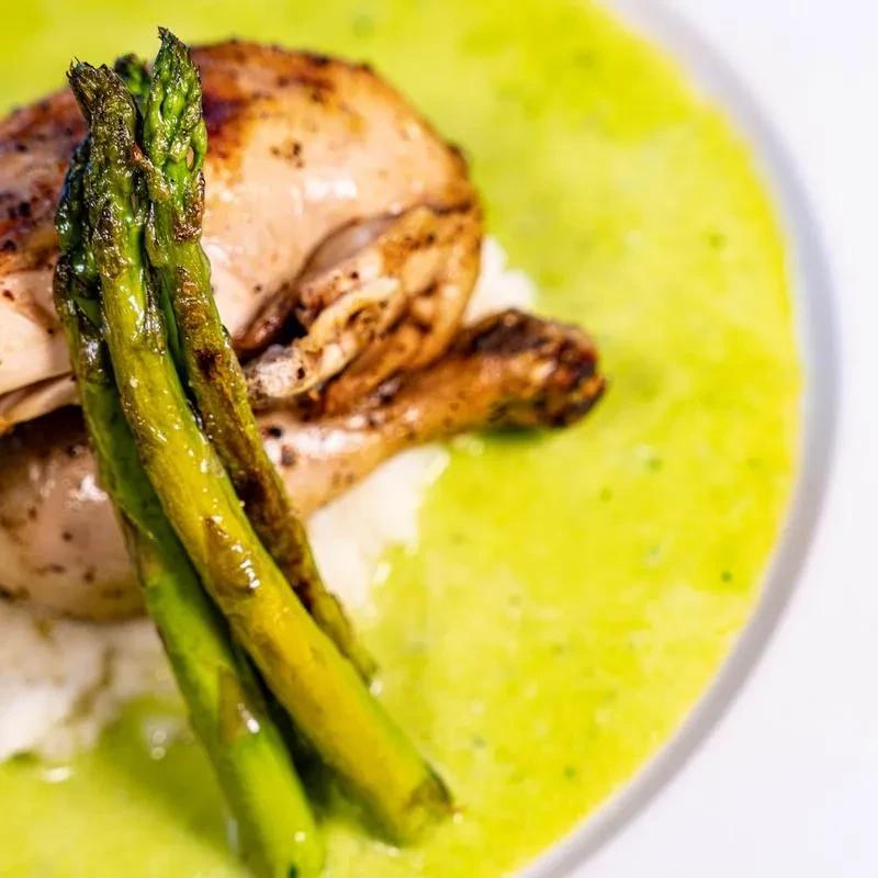 Plated roasted chicken, asparagus, white purée, and green sauce.