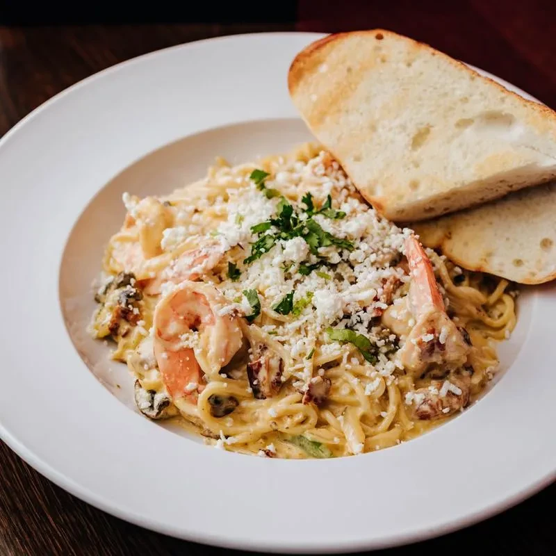 Overhead view of creamy shrimp pasta with cheese, herbs, and toast.