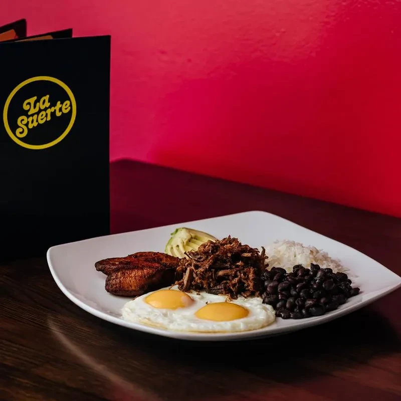 Plate with fried eggs, shredded meat, rice, beans, avocado, and plantain.