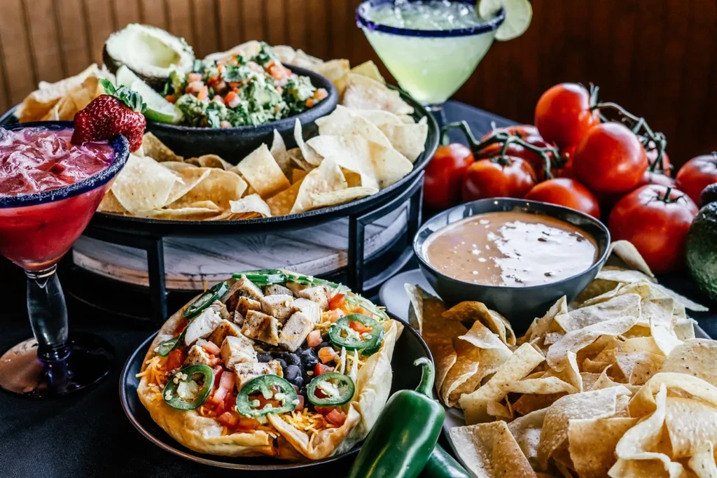 Vibrant spread of Mexican food: margaritas, chicken bowl, guacamole, queso.
