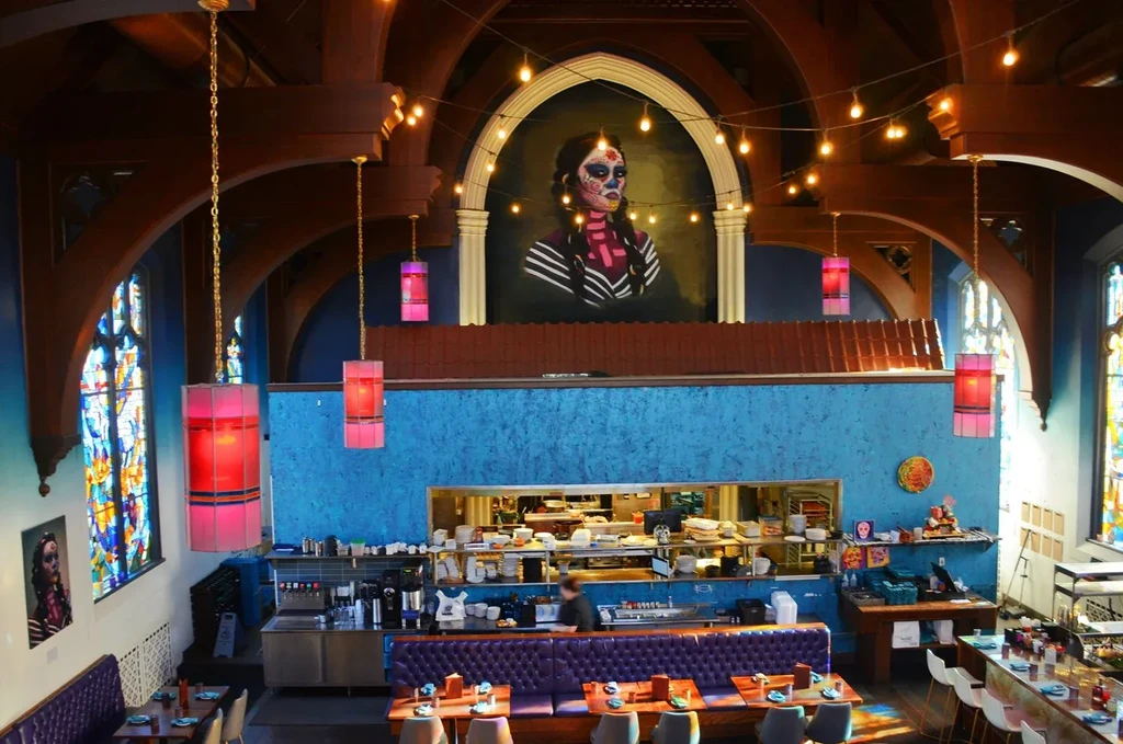 Vibrant restaurant interior with Day of the Dead mural, arched ceilings, and purple booths.