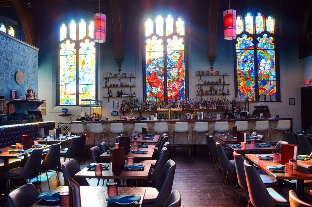 Repurposed church restaurant interior with bar and colorful stained-glass windows.