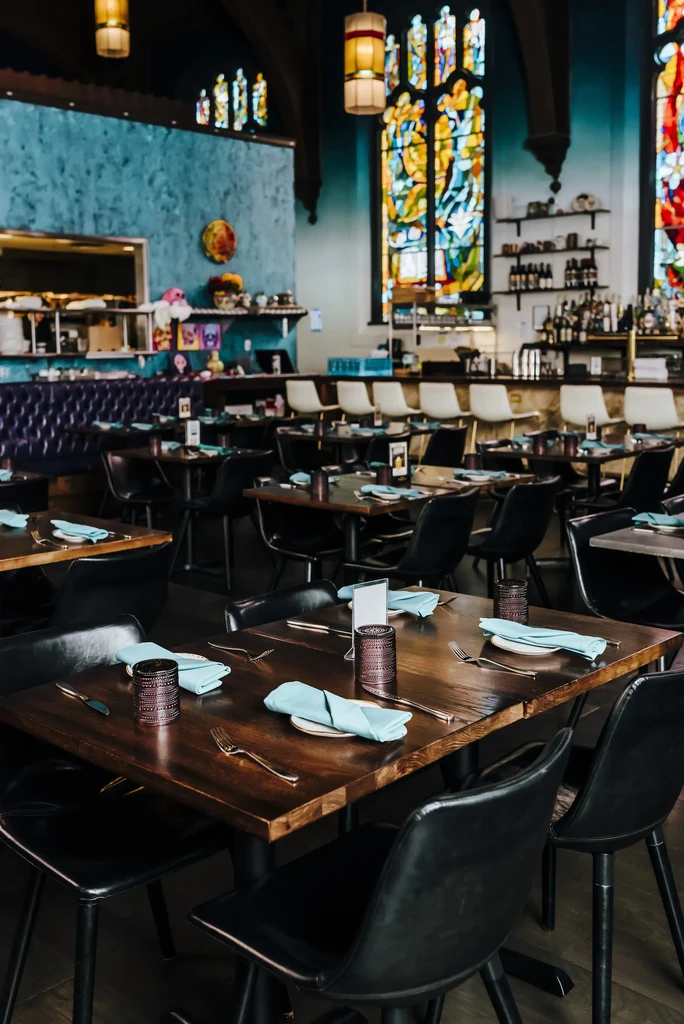 Stylish restaurant interior with stained glass, set tables, bar, and booths.