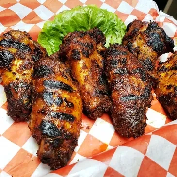 Dark grilled chicken wings in a checkered basket with lettuce.