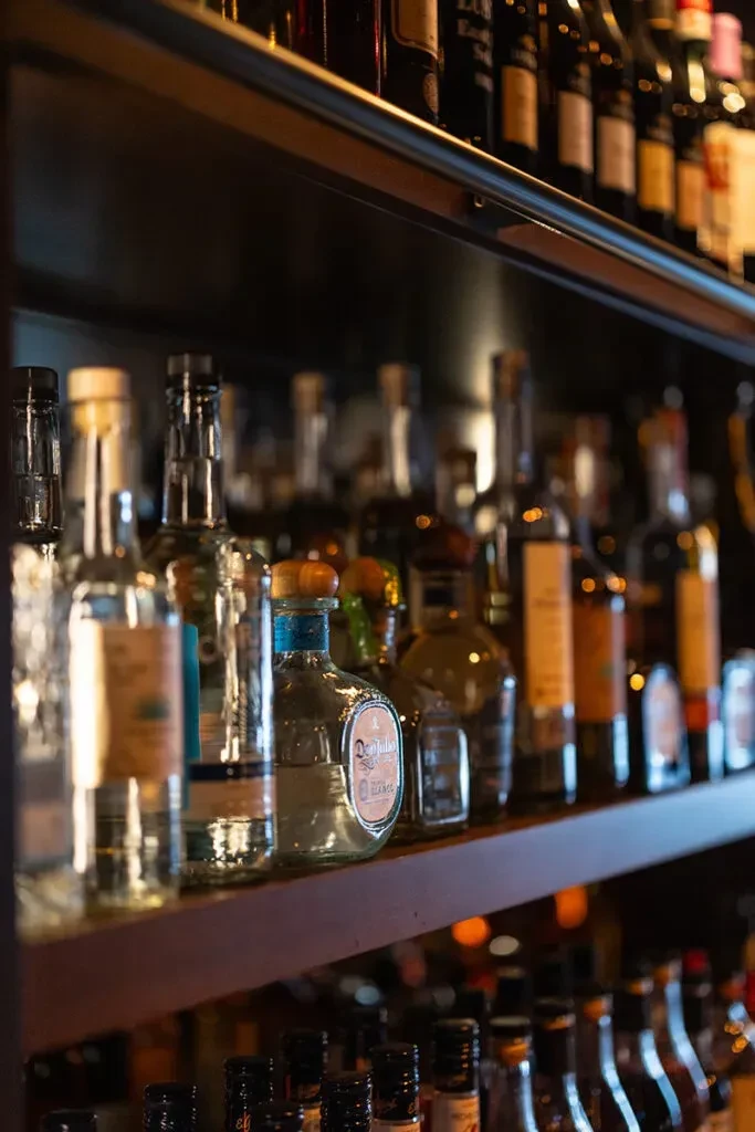 Dimly lit bar shelf stocked with various liquor bottles, Don Julio prominent.