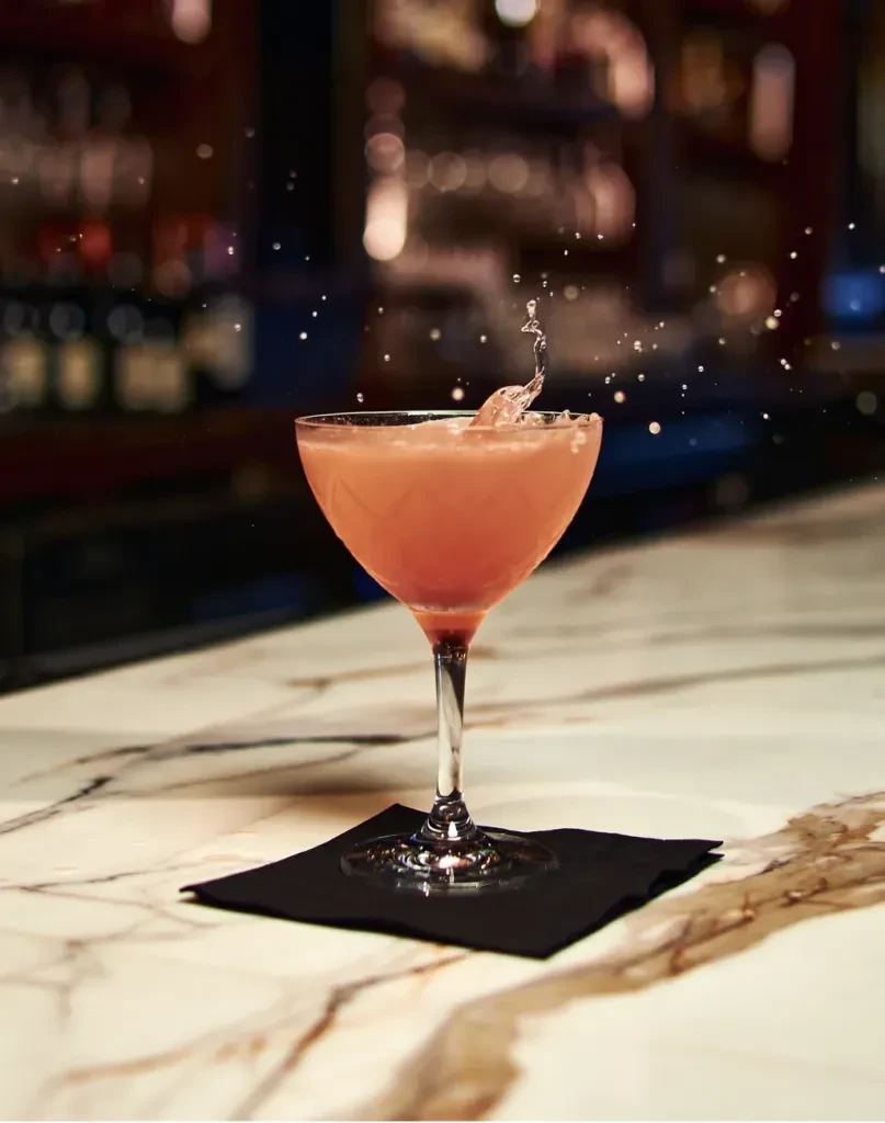 Peach cocktail in coupe glass with dramatic liquid splash on marble.