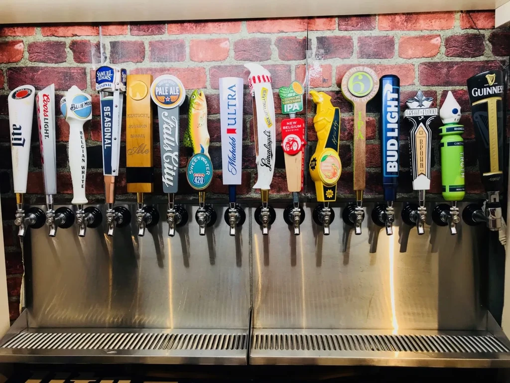 Colorful, branded draft beer taps line a rustic brick wall.
