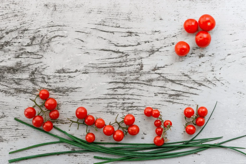 Fresh red cherry tomatoes and green chives on distressed white wood.