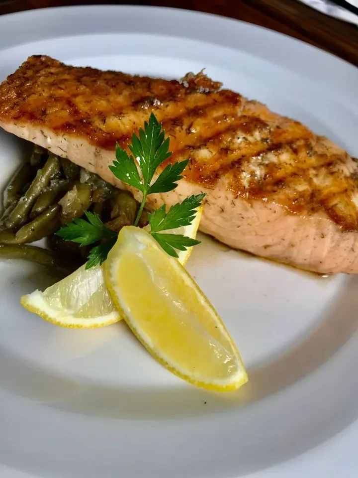 Grilled salmon fillet with green beans, lemon, and parsley on a white plate.