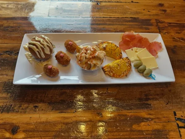White platter of various tapas: meat, cheese, pastries, croquettes, olives.