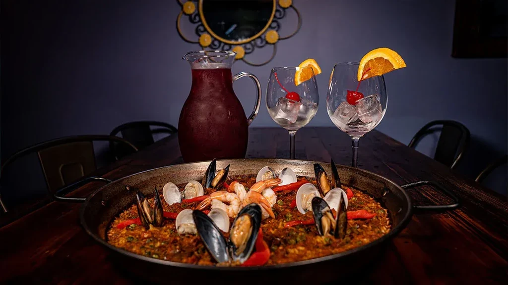 Seafood paella in a pan with sangria pitcher and garnished glasses.