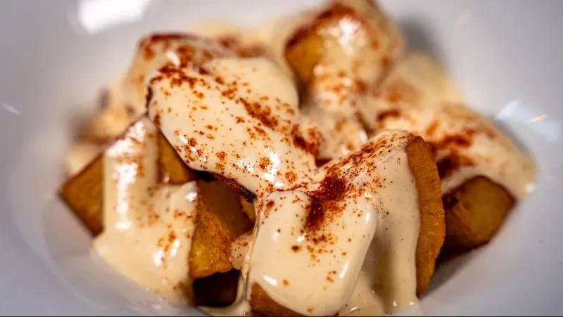 Fried potatoes with creamy sauce and reddish spice in a white bowl.