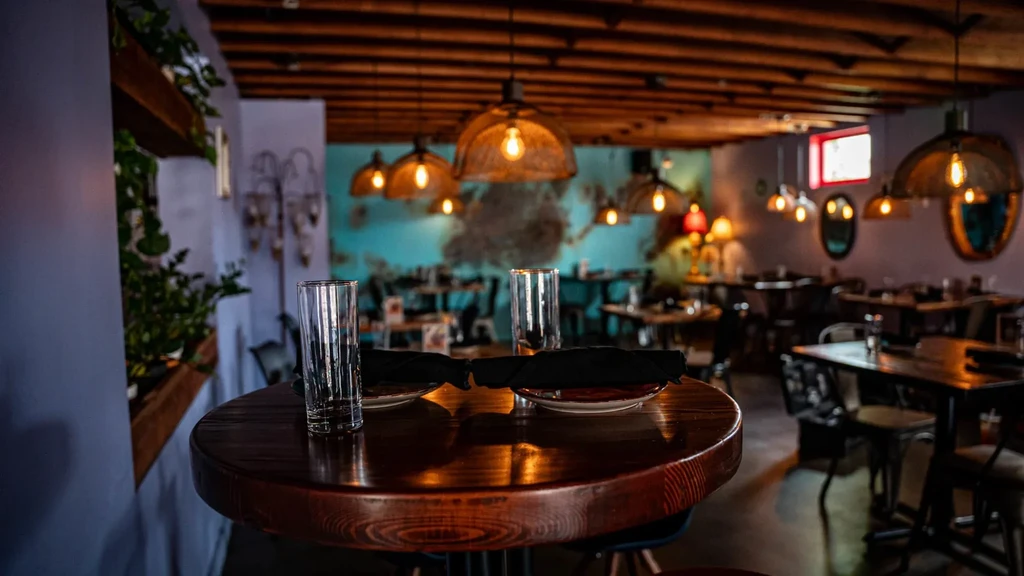 Warmly lit restaurant interior with wooden table, Edison bulbs, and accent wall.