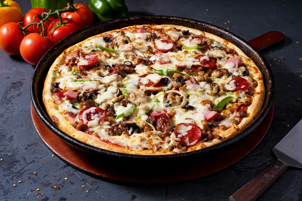 Deep-dish pizza with thick crust, abundant toppings, and fresh produce.