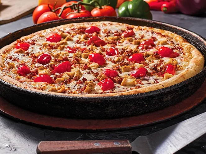 Deep-dish pizza with cheese, meat, and cherry tomatoes in cast-iron pan.