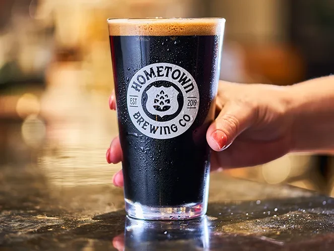 Hand holds a cold pint of dark beer from Hometown Brewing Co.