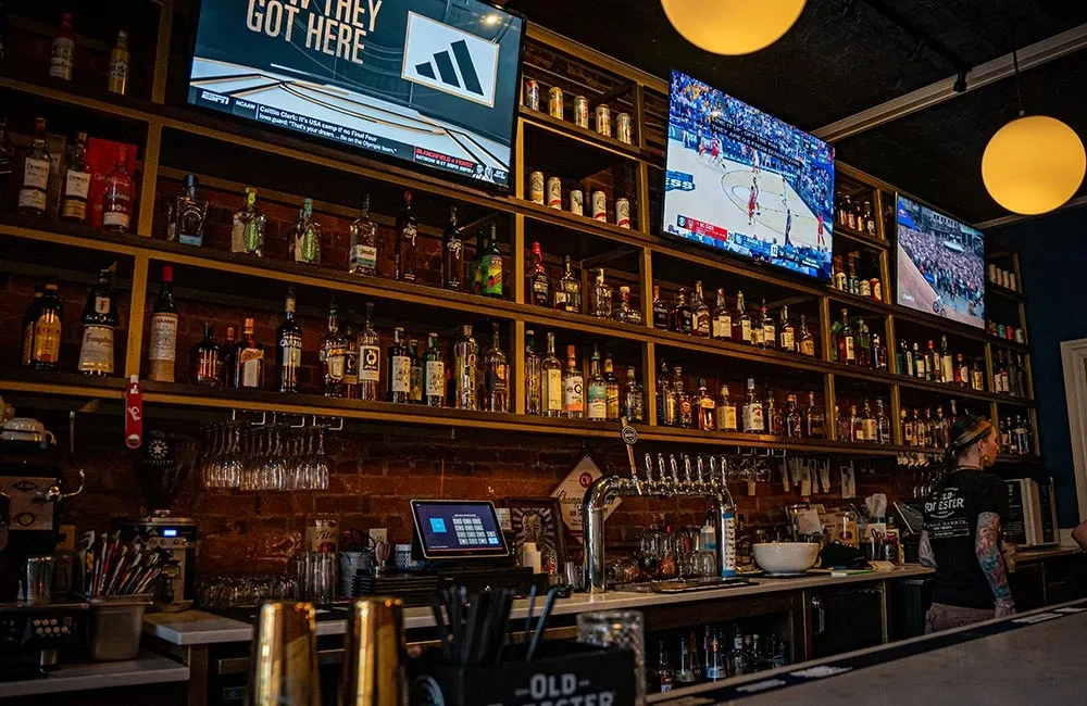 Vibrant sports bar interior with liquor wall, TVs, and bartender.